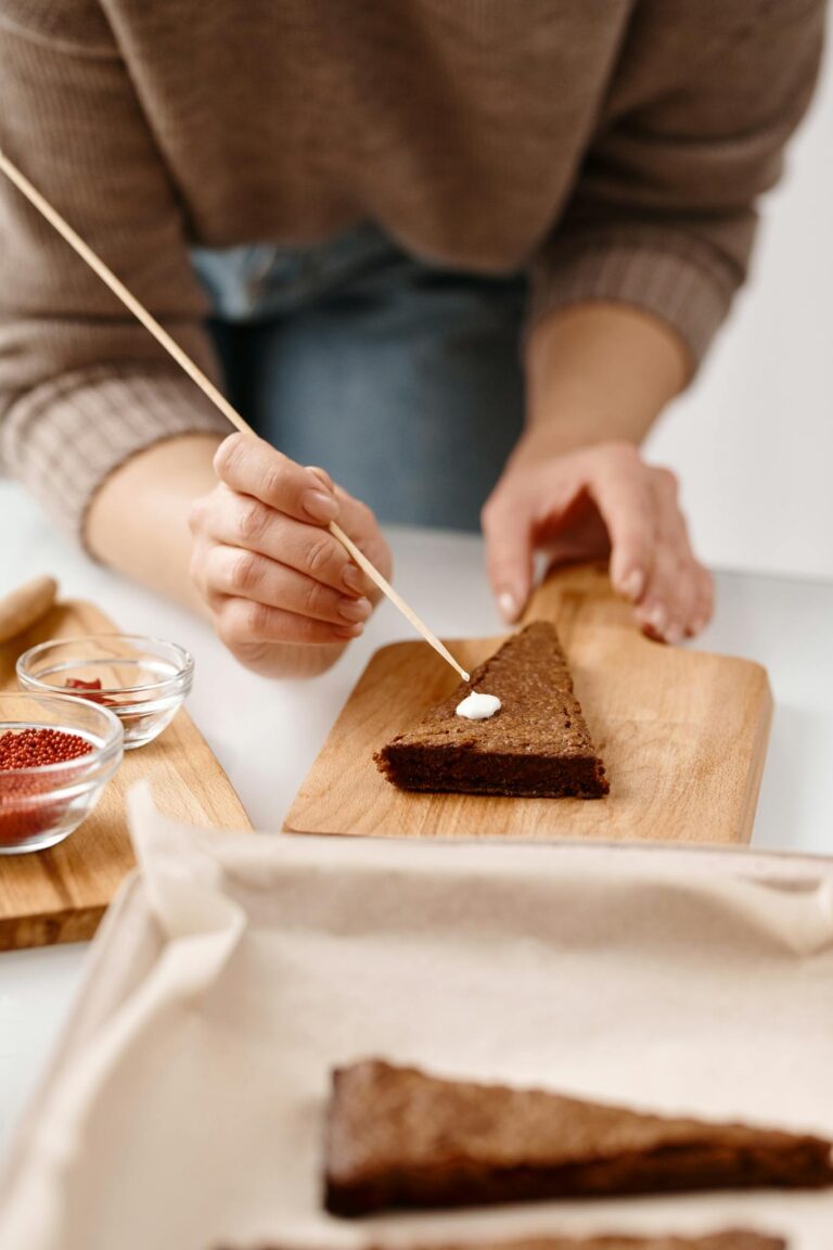 A person decorates a gingerbread slice with icing on a wooden board, showcasing festive preparation.