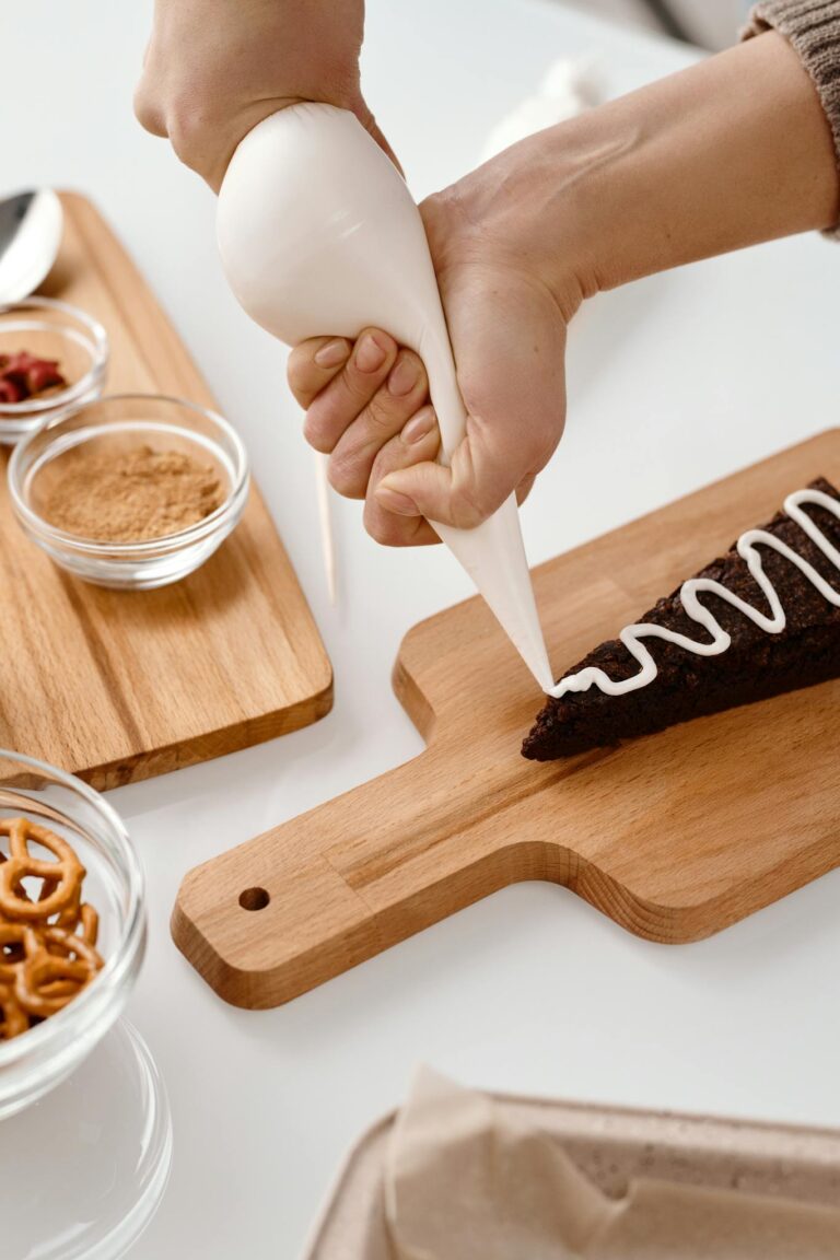 Hands decorating a chocolate cake with icing on a wooden board, creating festive details.